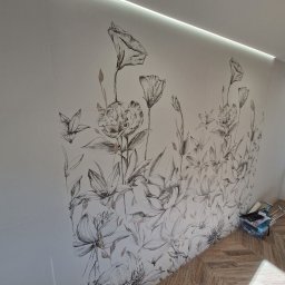 SEB-BUD - Ściana wykończona płytkami z motywem kwiatowym w odcieniach szarości, z widocznym oświetleniem LED i fragmentem podłogi z parkietu ułożonego w jodełkę.