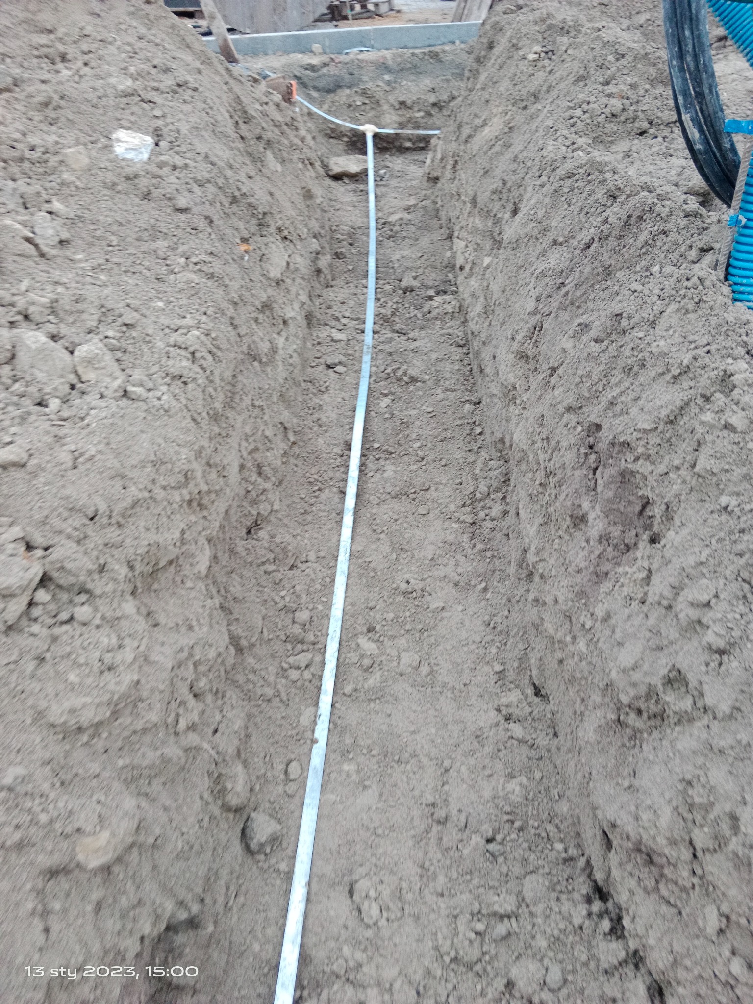 Wykop w ziemi z ułożoną rurą osłonową, widoczne ślady po wykopie i ziemia po bokach.