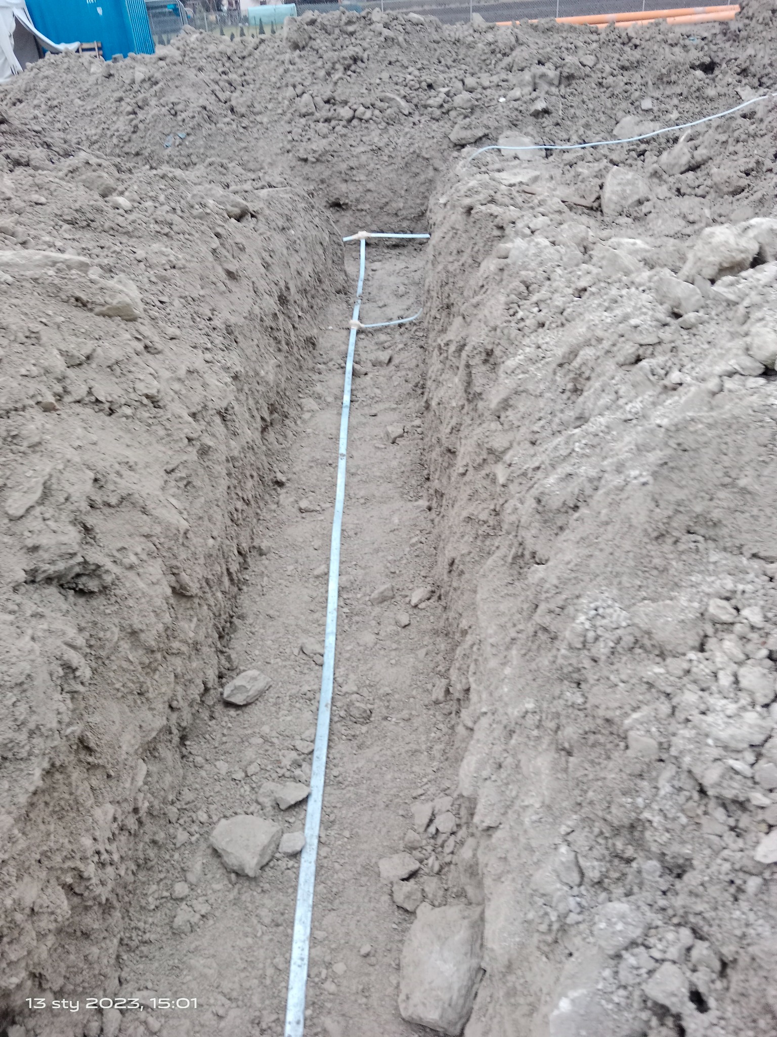 Wykop w ziemi z ułożoną rurą, prawdopodobnie do instalacji podziemnej, widoczne ślady pracy ziemnej i pryzma ziemi w tle.