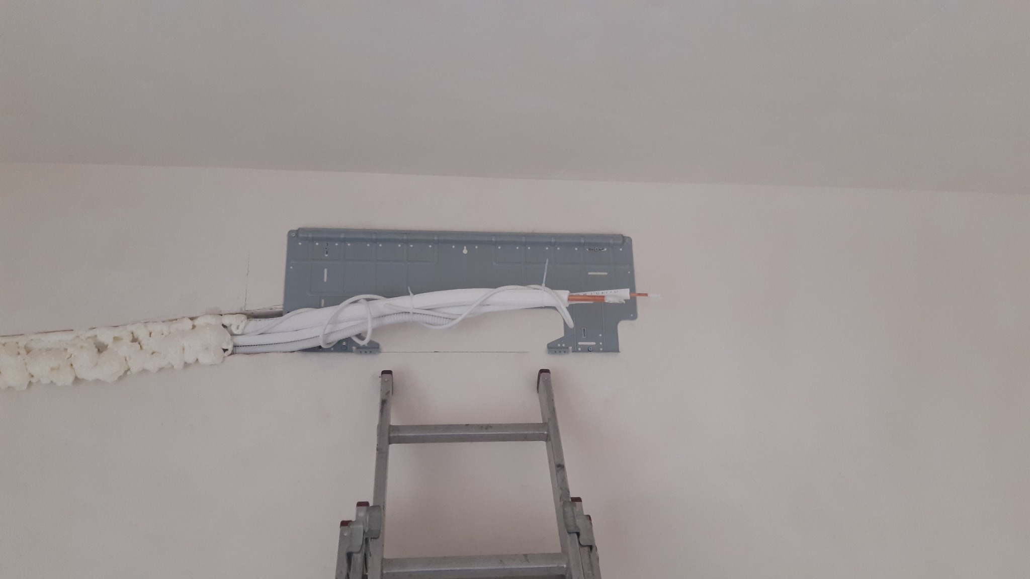 Montaż klimatyzacji: wspornik jednostki wewnętrznej przymocowany do ściany, przewody w izolacji piankowej prowadzone w bruździe, drabina rozstawiona pod spodem.