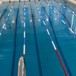 ArtPool Yaroslav Konakh - Kryty basen sportowy z torami oddzielonymi linami w kolorach czerwonym, białym i niebieskim, widok z perspektywy skraju basenu.