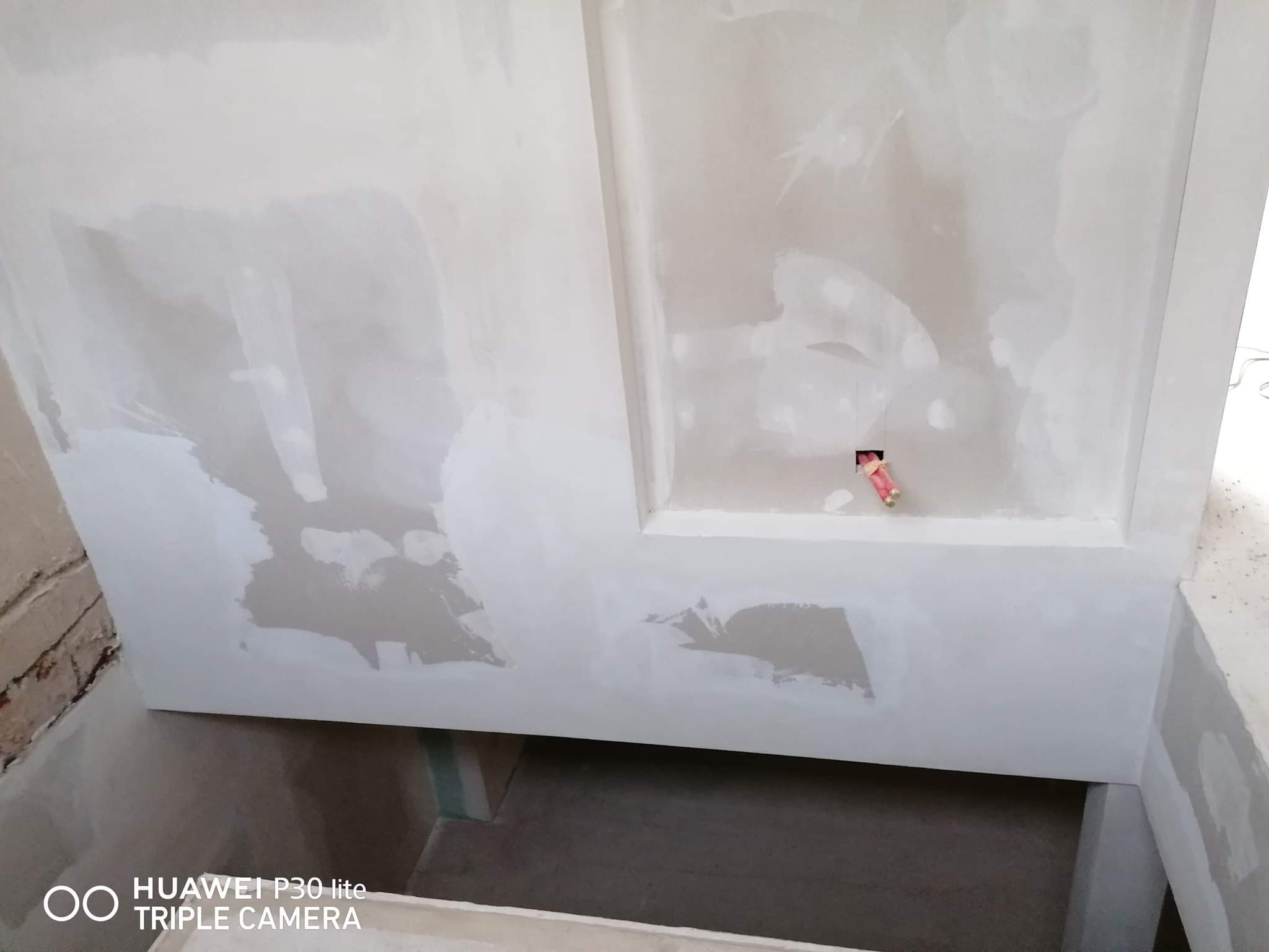 Ściana z wnęką w trakcie szpachlowania, widoczne niedoskonałości i wystające przewody elektryczne.