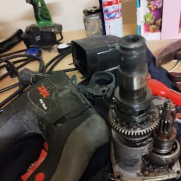 Rozłożony mechanizm wiertarki udarowej Skil 650 Watt, obok narzędzia akumulatorowe, śrubokręt i smar WD-40, w tle zabawka.