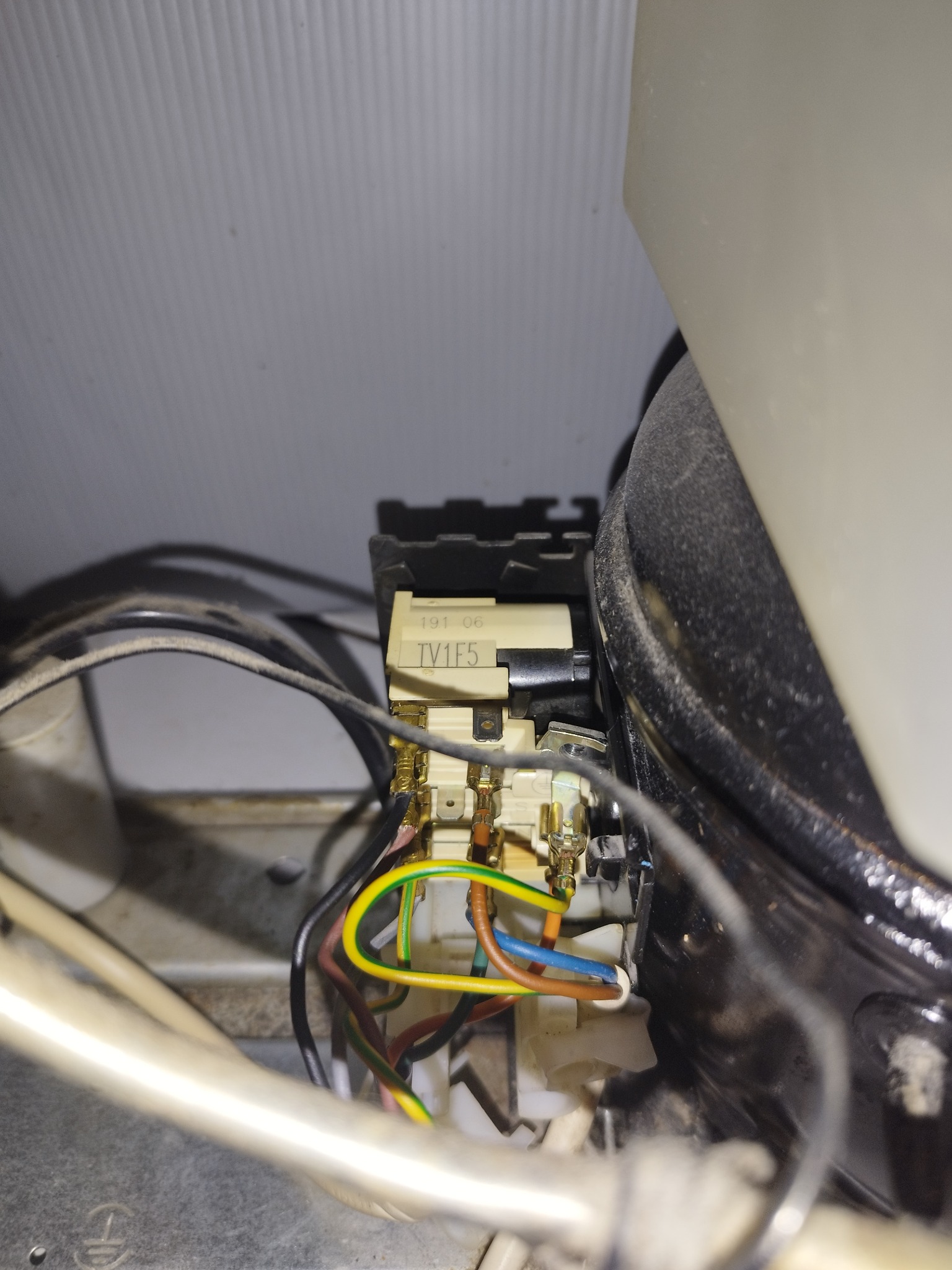 Detal widoczny z tyłu lodówki, przedstawiający podłączenie elektryczne z kostką TV1F5 i kolorowymi kablami: żółto-zielonym, niebieskim, brązowym, czarnym i innymi, wewnątrz obudowy.