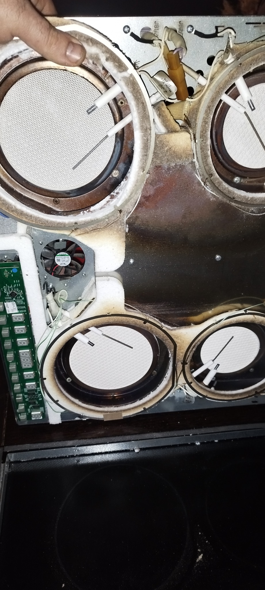 Wnętrze płyty indukcyjnej z widocznymi elementami grzejnymi, elektroniką sterującą i śladami użytkowania, w trakcie diagnozy lub naprawy.