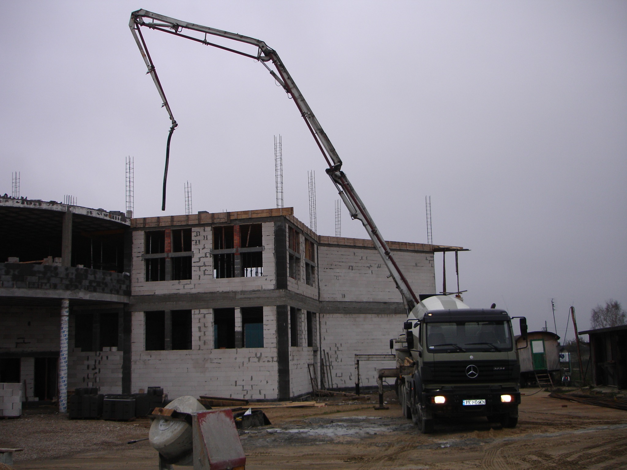 Budowa budynku z betonu komórkowego: widok na dwupiętrową konstrukcję w stanie surowym otwartym, z dźwigiem do betonu i betoniarką na placu budowy