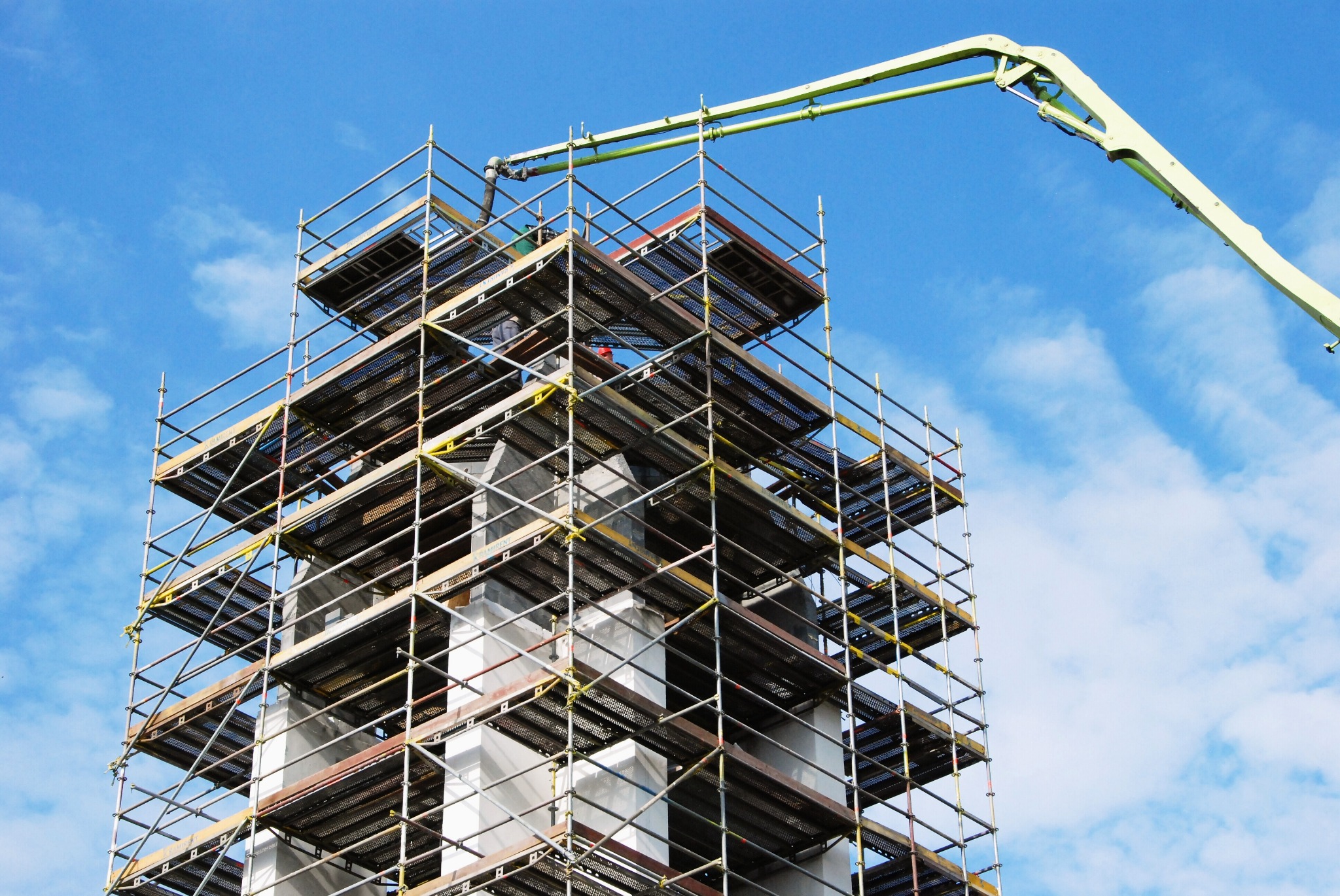 Wznoszenie ścian budynku z betonu na rusztowaniu z podnośnikiem do betonu w Żukowie, na tle błękitnego nieba.