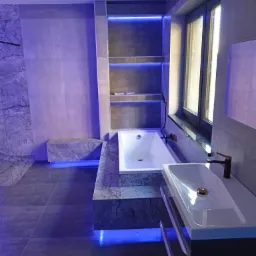 Nowoczesna łazienka z marmurowymi akcentami, podświetleniem LED w półkach i pod wanną, oraz armaturą w kolorze mosiądzu.