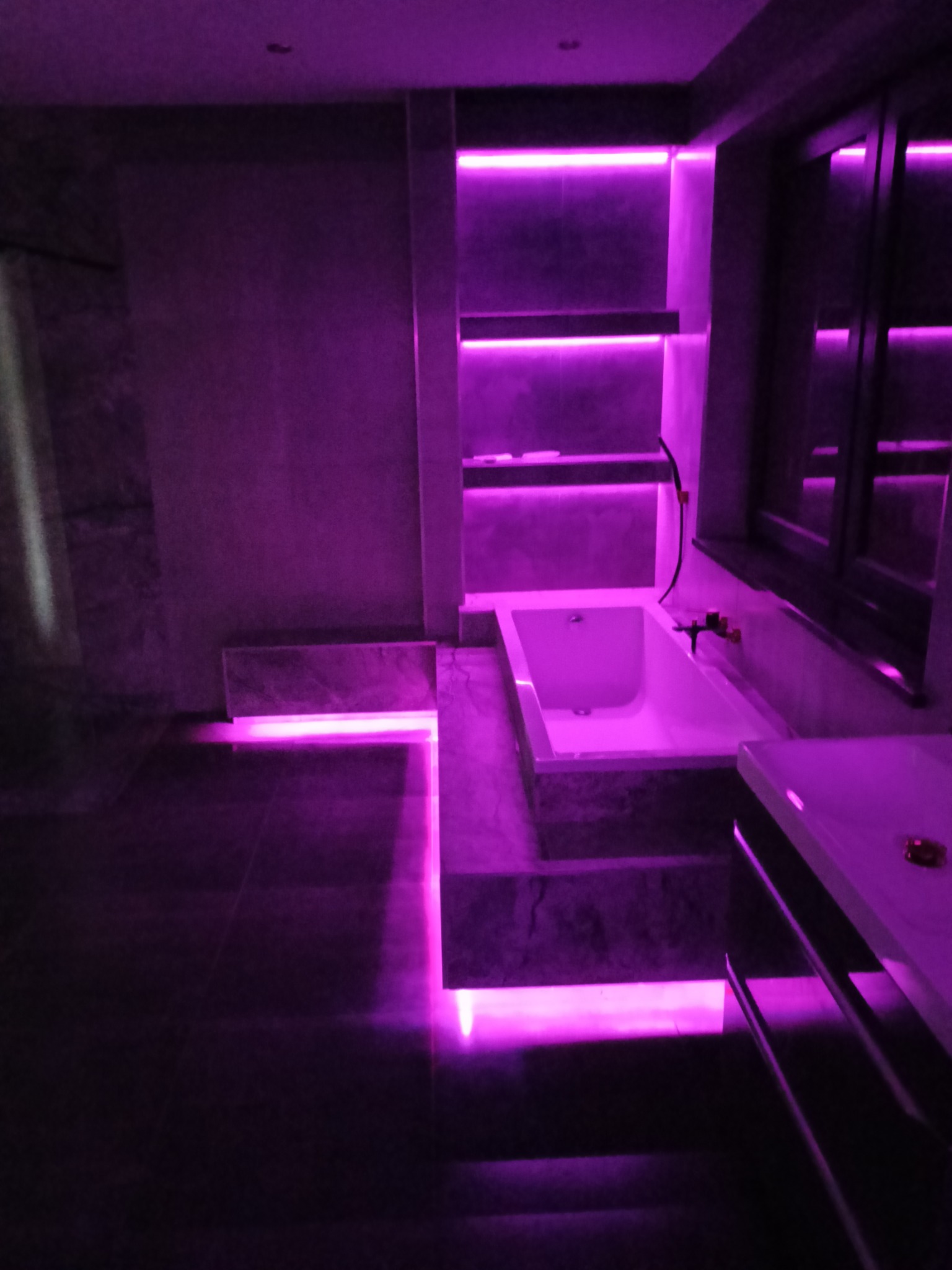 Nowoczesna aranżacja łazienki w Siemianowicach Śląskich z podświetleniem LED w kolorze fioletowym, obejmująca wannę, półki wnękowe i podłogę.