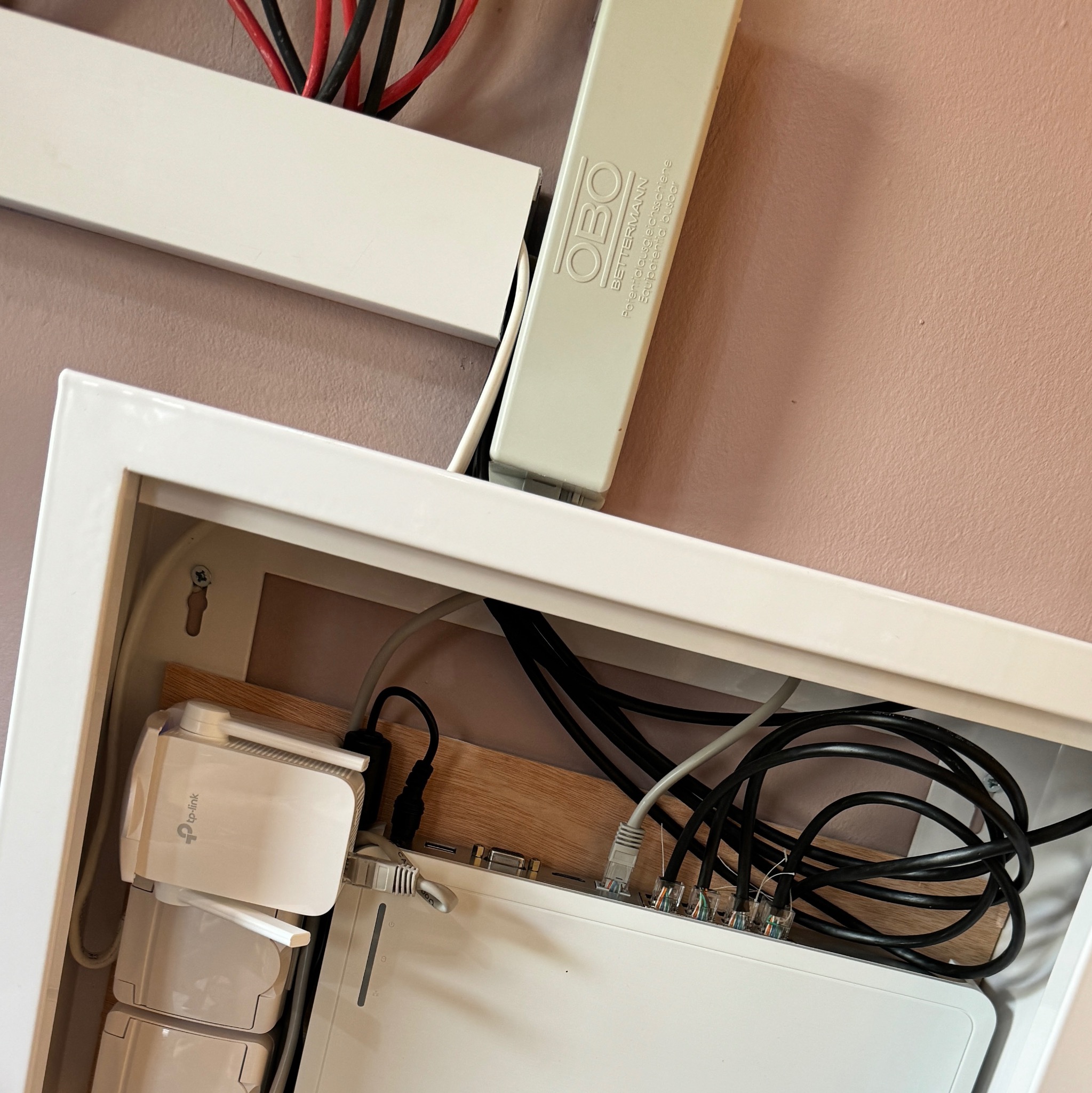 Wewnętrzna szafka z routerem i wzmacniaczami sygnału WiFi TP-Link, widoczne kable oraz listwa OBO Betterman, instalacja sieci komputerowej w domu.