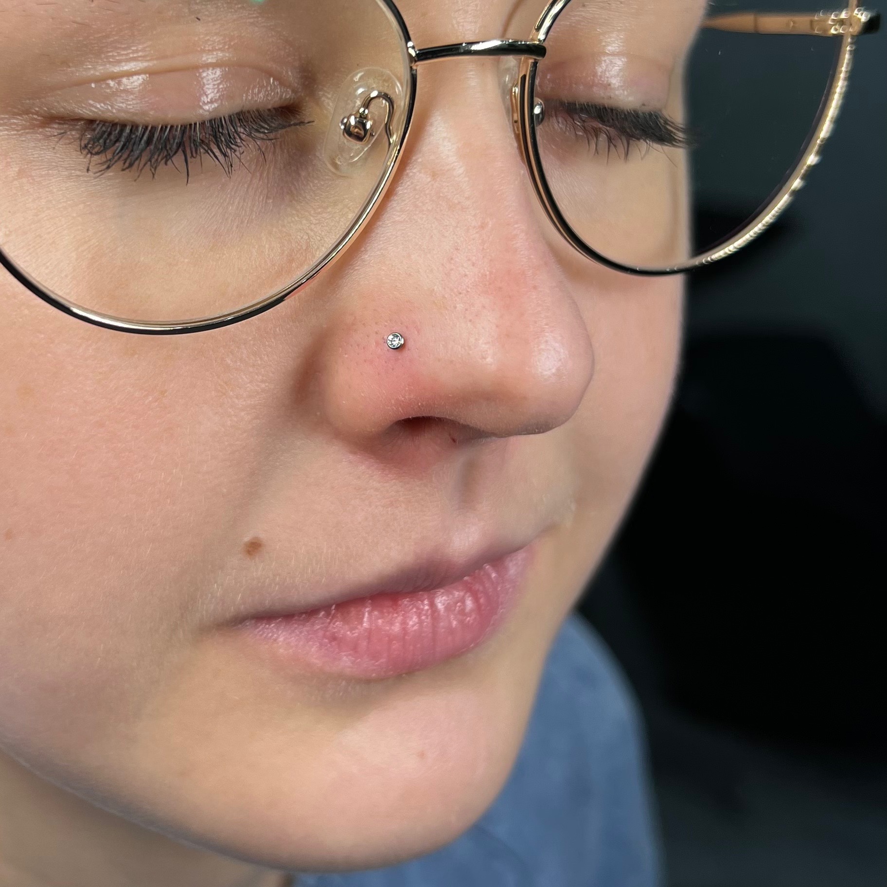 Zbliżenie na kobiecą twarz w okularach z delikatnym piercingiem nosa z małym, błyszczącym kamieniem.