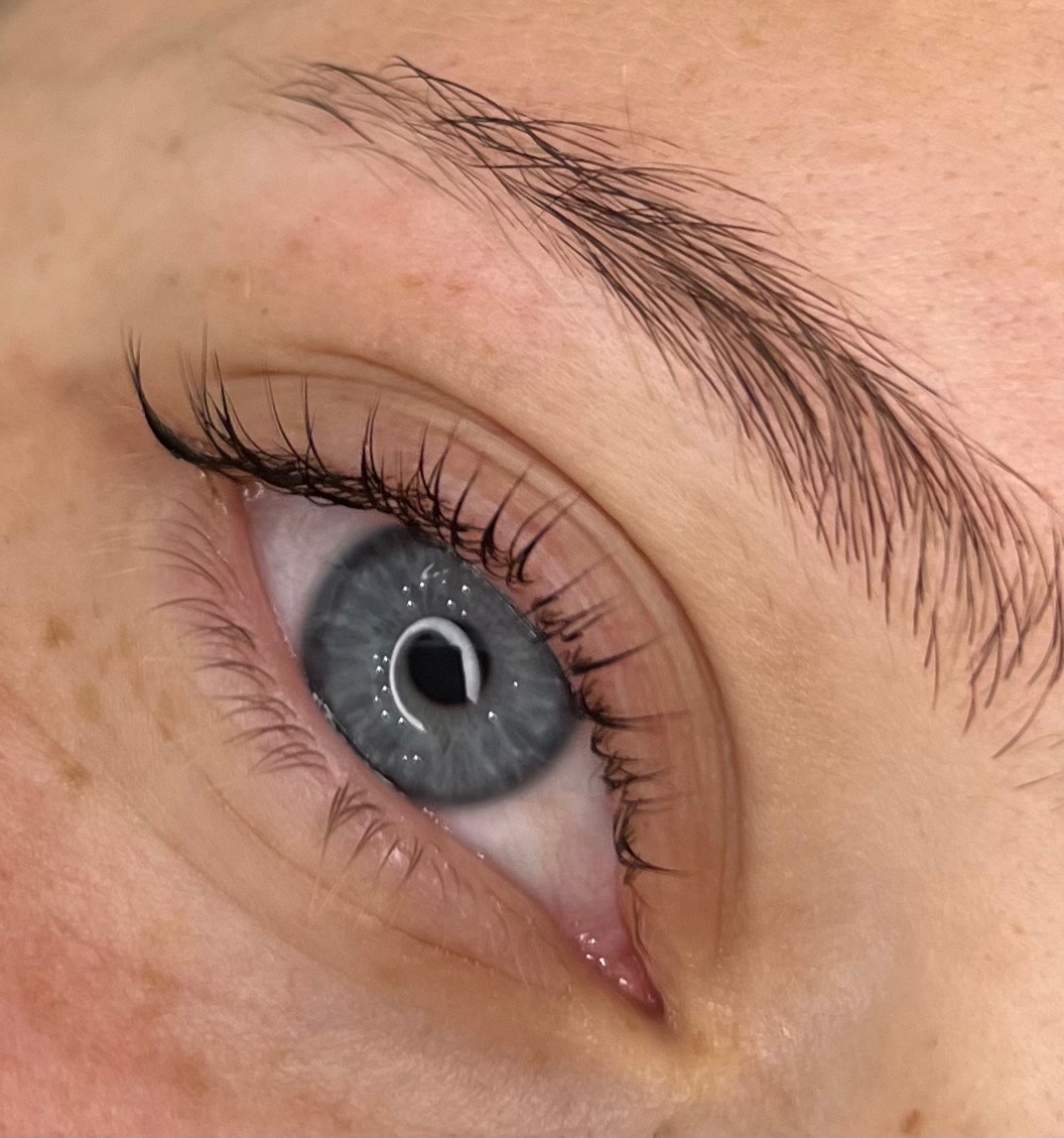 Zbliżenie na oko z szarym tęczówką i widocznymi, świeżo przedłużonymi rzęsami oraz wyregulowanymi brwiami.