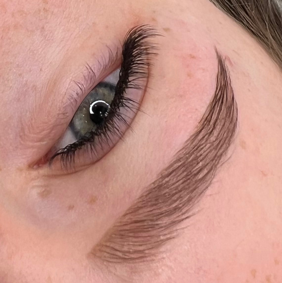 Zbliżenie na oko z przedłużonymi rzęsami i świeżo wyregulowanymi brwiami, widoczne drobne piegi na skórze.