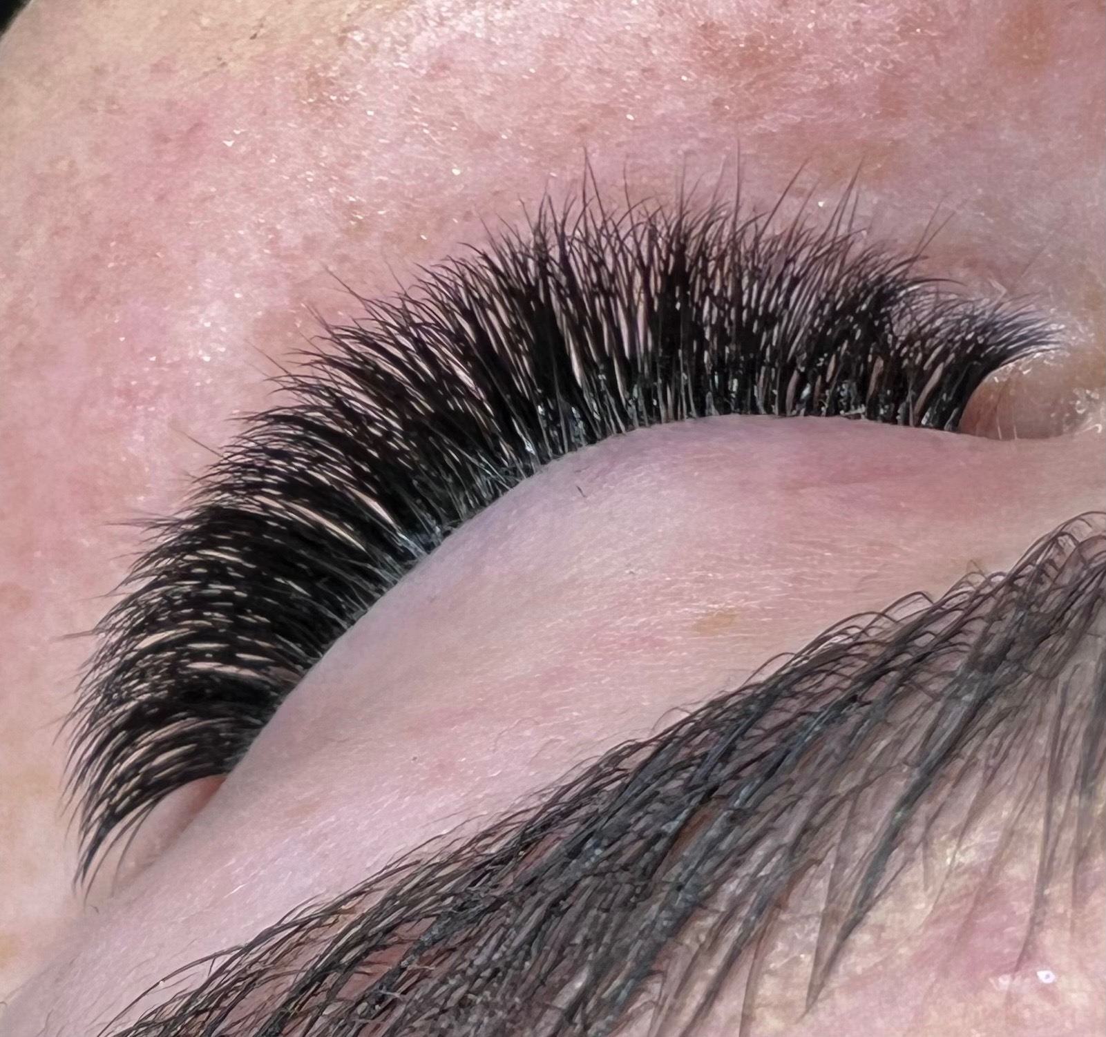 Zbliżenie na oko z gęstymi, czarnymi, przedłużonymi rzęsami, widoczna skóra powieki i brwi.