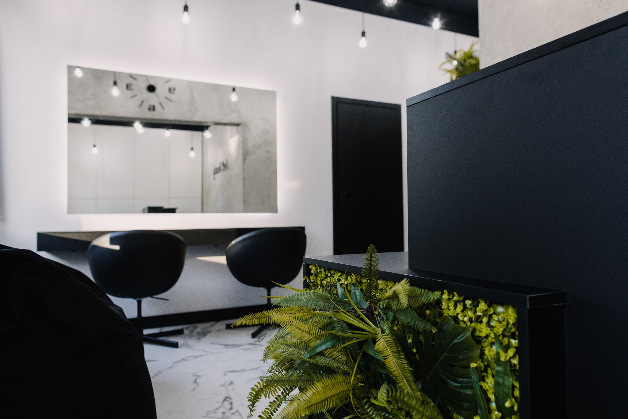 Nowoczesne wnętrze salonu: minimalistyczne stanowisko z lustrem podświetlonym diodami LED, czarne krzesła obrotowe, dekoracja z zielonych roślin w geometrycznej obudowie, marmurowa podłoga.