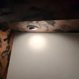 Dekoracyjna belka stropowa w Przyłęku, z efektem postarzanego drewna i wpuszczonym oświetleniem punktowym, oświetlająca gładką, jasną ścianę.