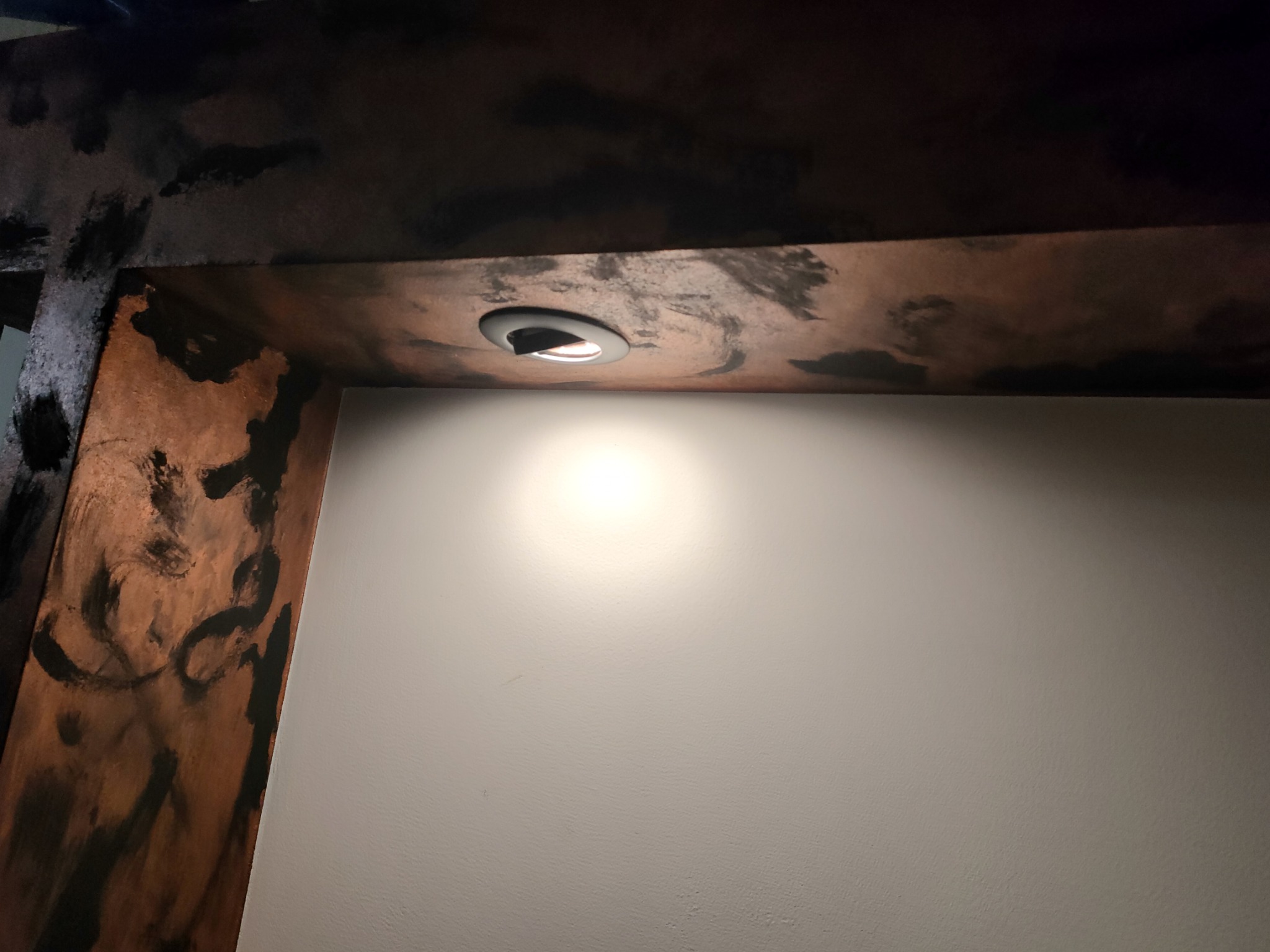 Dekoracyjna belka stropowa w Przyłęku, z efektem postarzanego drewna i wpuszczonym oświetleniem punktowym, oświetlająca gładką, jasną ścianę.