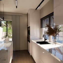 Nowoczesna kuchnia z marmurowym blatem, czarnym zlewem i minimalistycznym oświetleniem. Widok na zewnątrz przez okno z żaluzjami i dekoracyjną trawą w wazonie.