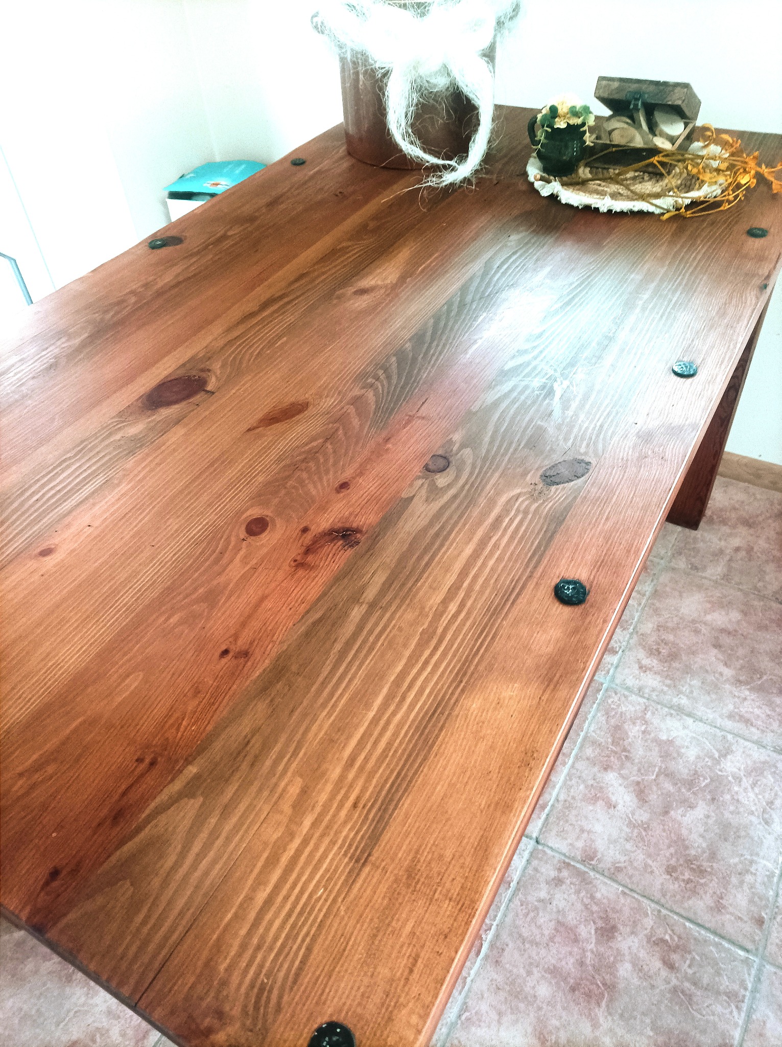 Rustykalny drewniany stół z ciemnymi okuciami, ozdobiony kompozycją kwiatową i dekoracjami w Łomży, ustawiony na tle płytek podłogowych.