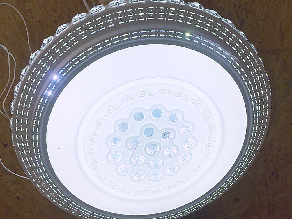 Okrągła lampa sufitowa LED z dekoracyjnymi kryształkami na obrzeżach i wzorem na środku, widok od dołu.