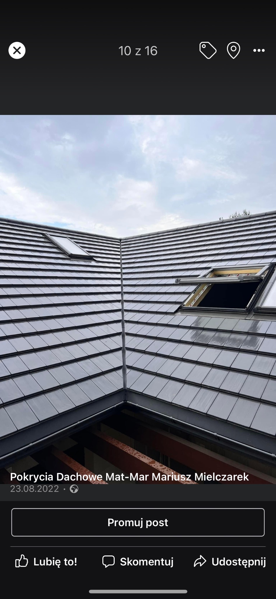 Nowe, błyszczące, szare dachówki ceramiczne z dwoma oknami dachowymi, jedno z nich otwarte, widok z dołu na fragment konstrukcji więźby dachowej.