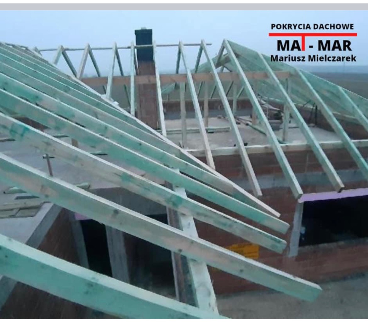 Wznoszenie konstrukcji drewnianej dachu z widocznym kominem murowanym z cegły, lekko zamglone tło.