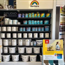 Półki w sklepie budowlanym wypełnione puszkami farb marek Beckers i Tikkurila, w tym farby do ścian, kuchni, łazienek, drewna i metalu, oraz reklama farby do płytek ceramicznych.