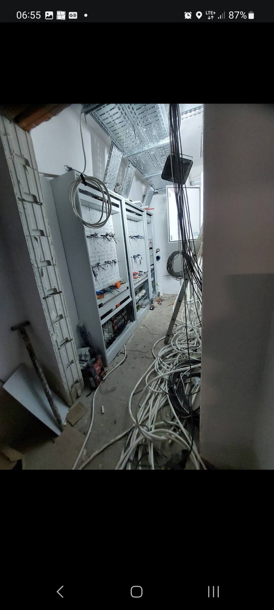 Dwa otwarte panele elektryczne w trakcie montażu w surowym pomieszczeniu, widoczne kable, drabina i narzędzia.