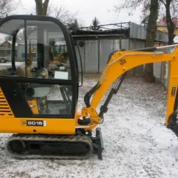 Żółta mini koparka JCB 8015 na śniegu, widok z boku, kabina zamknięta, łyżka skierowana w dół.