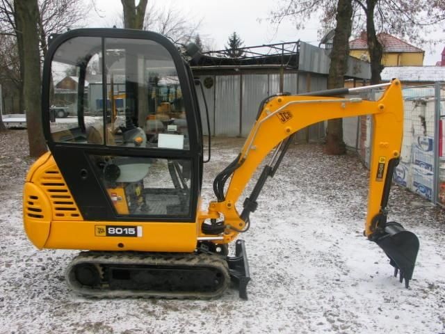 Żółta mini koparka JCB 8015 na śniegu, widok z boku, kabina zamknięta, łyżka skierowana w dół.