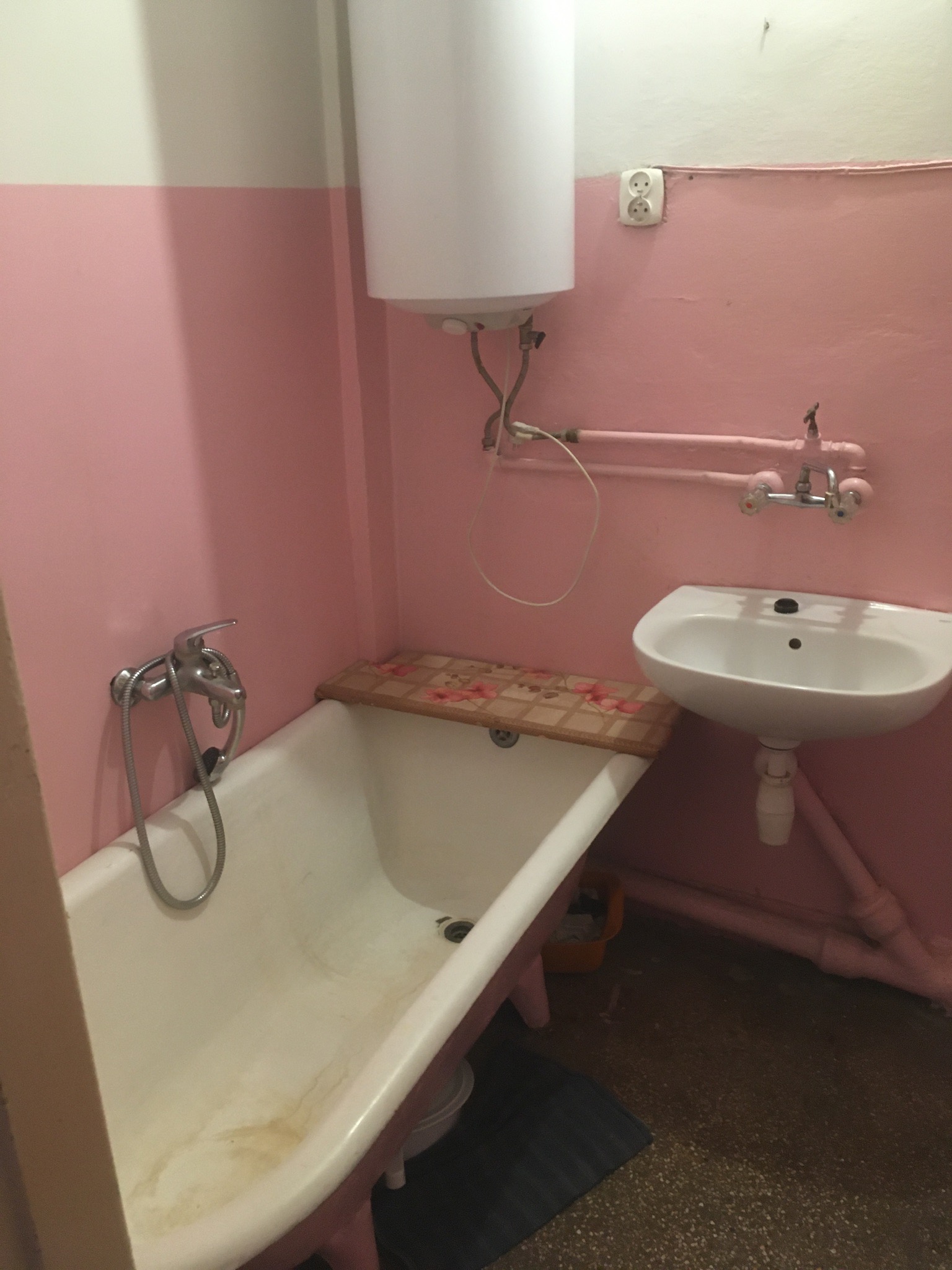 Łazienka w bloku z różowymi ścianami: wanna z drewnianą nakładką, umywalka na postumencie i bojler.