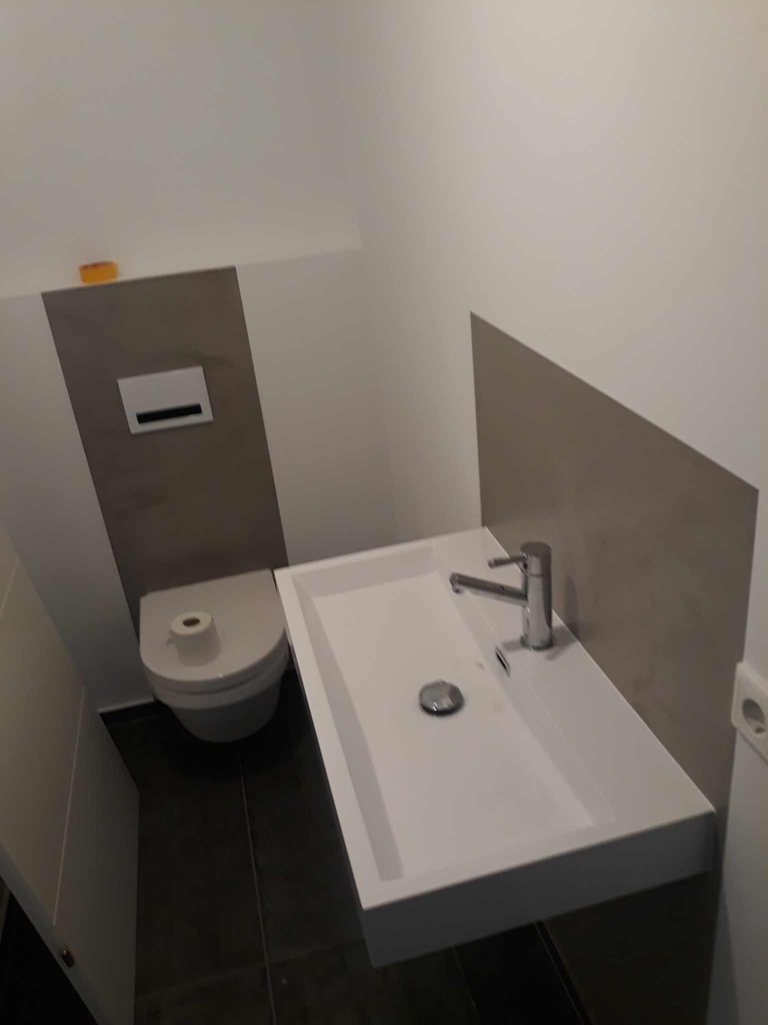 Nowoczesna, minimalistyczna łazienka z wiszącą toaletą i prostokątną umywalką nablatową, wykończona w odcieniach bieli i szarości, z akcentem w postaci kostki mydła na półce.