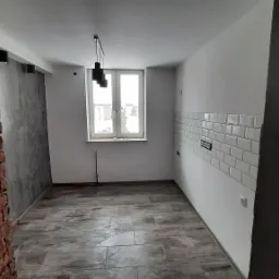 Surowe wnętrze po remoncie: ceglana ściana, szare tynki dekoracyjne, białe płytki metra na ścianie, drewnopodobna podłoga, czarne lampy wiszące