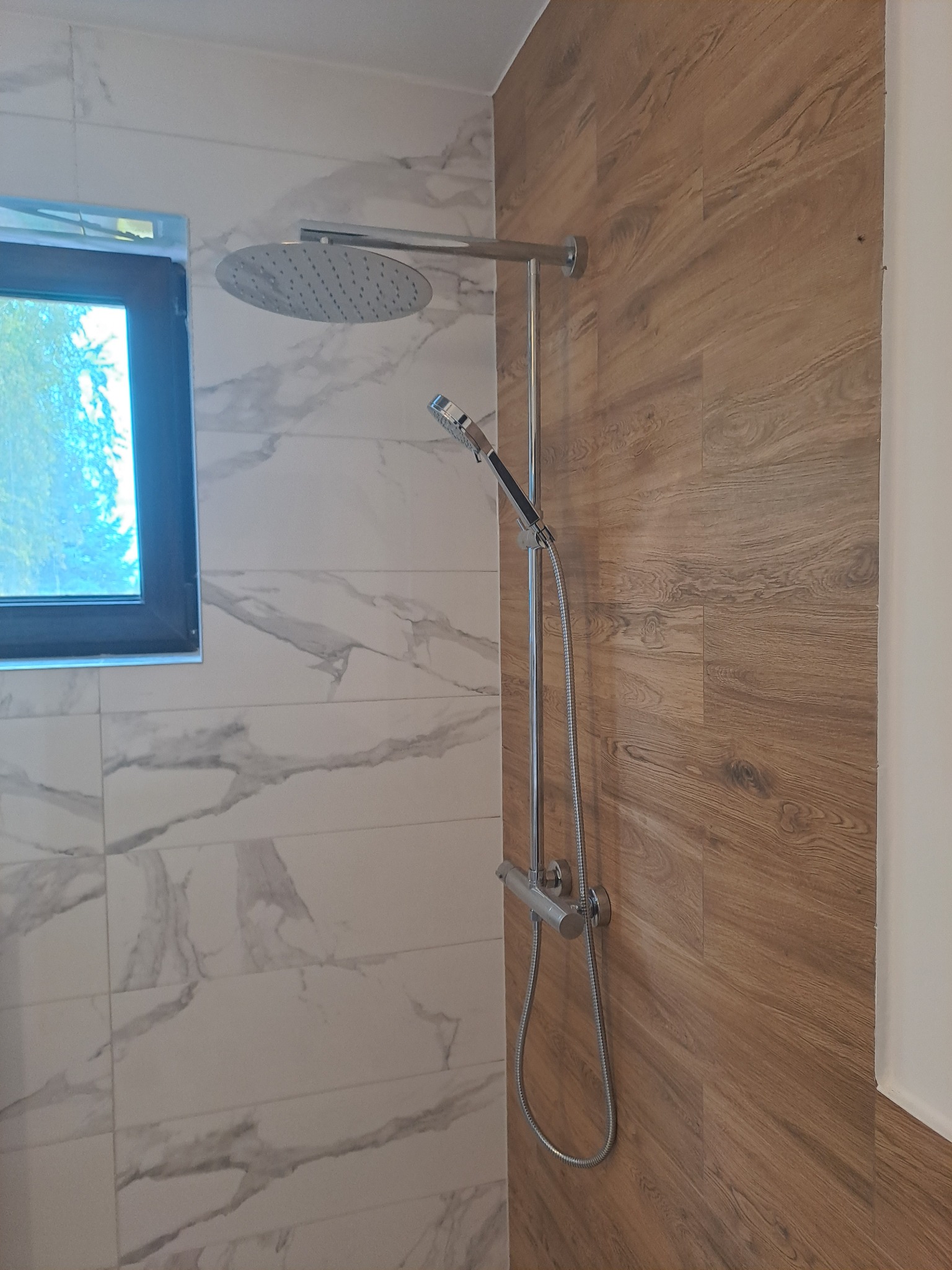 Nowoczesna kabina prysznicowa z deszczownicą i panelem natryskowym, wykończona płytkami imitującymi marmur i drewno.