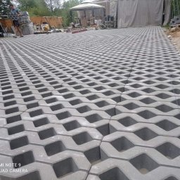 Mój raj - Ułożona nawierzchnia z ażurowych betonowych płyt w kształcie fal, widoczne niebieskie sznurki wyznaczające linię, w tle osoba przenosi kolejne elementy, teren budowy i zadaszenie.