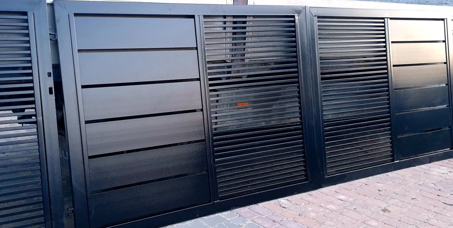 Nowoczesna, przesuwna brama wjazdowa z poziomymi panelami i szczebelkami, pomalowana na ciemny, metaliczny kolor, z widoczną kostką brukową u podstawy.