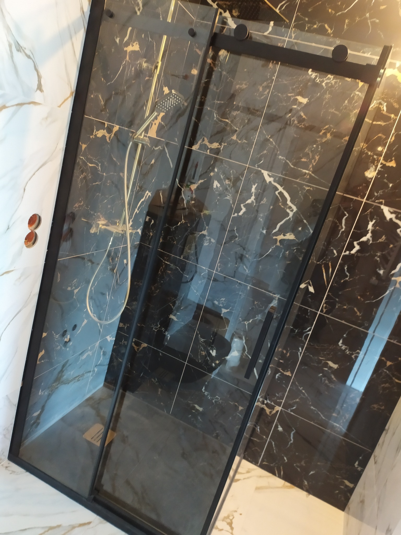 Nowoczesna kabina prysznicowa z czarnymi ramami i marmurowymi płytkami w odcieniach czerni i bieli, widok ukośny z góry.