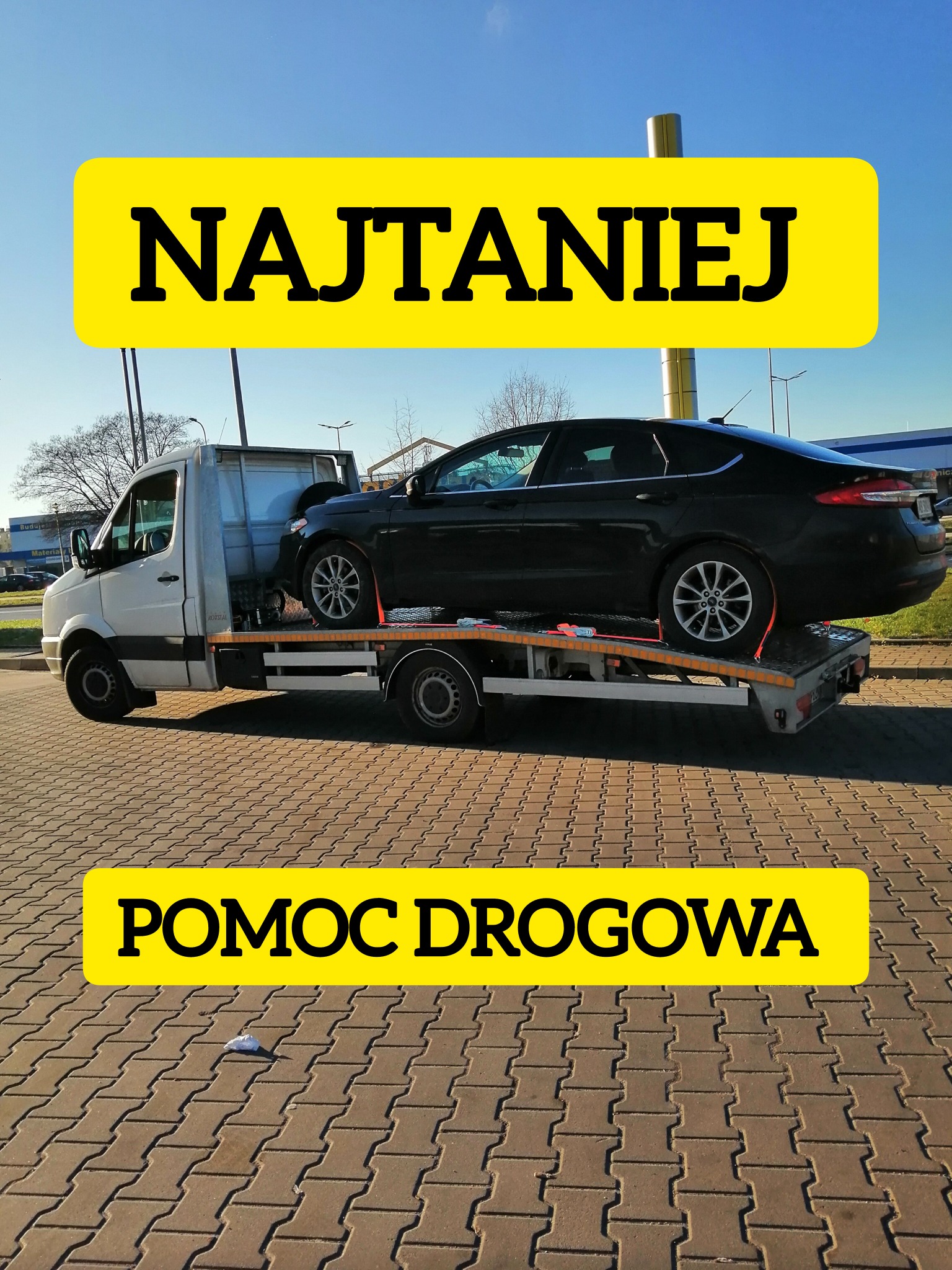 Laweta z czarnym samochodem osobowym Ford na platformie transportowej, zabezpieczonym czerwonymi pasami, na brukowanym parkingu w słoneczny dzień.