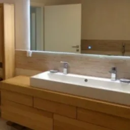 Nowoczesna łazienka z drewnianą szafką pod umywalką, podświetlanym lustrem i wysoką szafką boczną z otwartymi półkami.