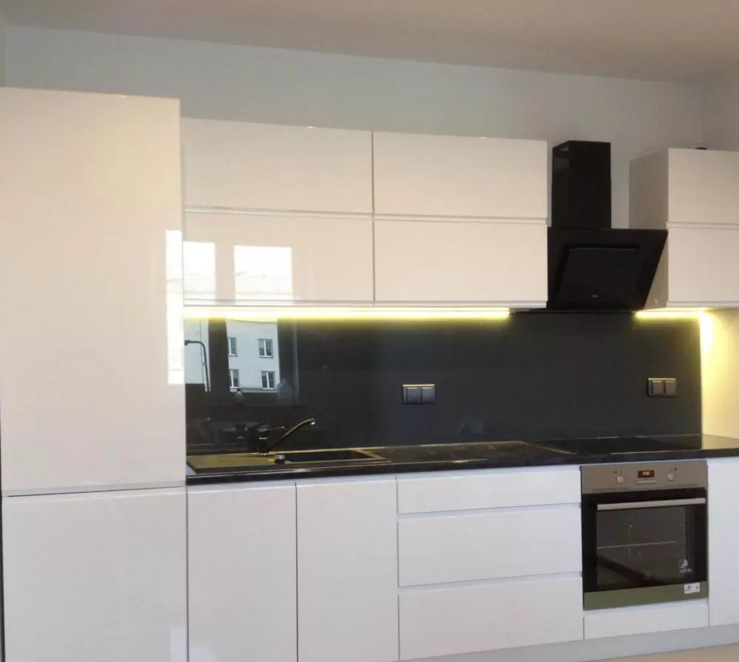 Nowoczesna kuchnia z białymi, lakierowanymi frontami, czarnym blatem i panelem szklanym, oświetleniem LED podszafkowym i czarnym okapem.