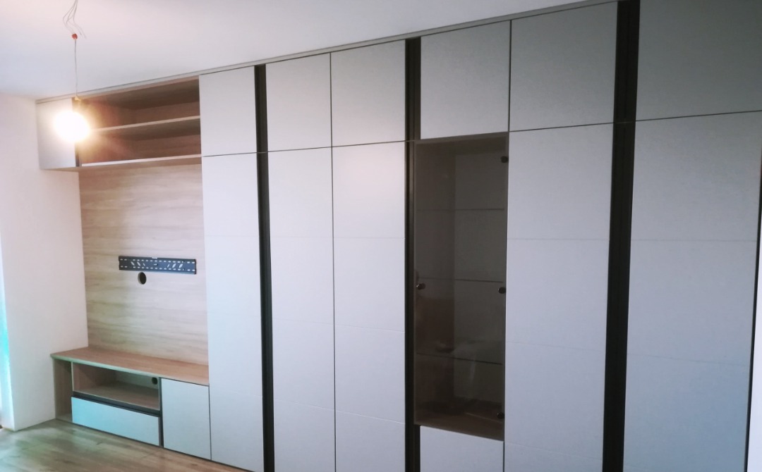 Zabudowa ściany z szafami z białymi frontami, czarnymi wstawkami i szklaną witryną, drewniana ściana z półkami i uchwytem na telewizor.