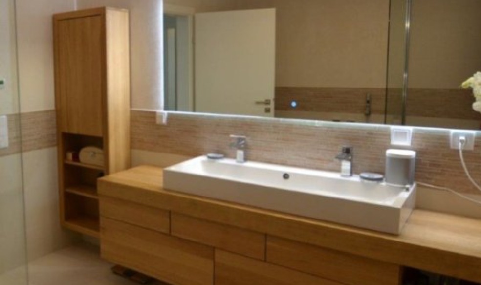 Nowoczesna łazienka z drewnianą szafką pod umywalką, podświetlanym lustrem i wysoką szafką boczną z otwartymi półkami.