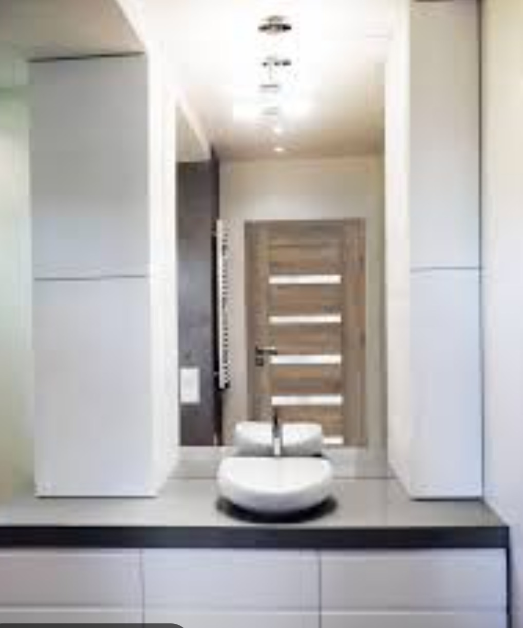 Nowoczesna łazienka z umywalką nablatową, drewnianymi drzwiami z poziomymi przeszkleniami i zabudową meblową z białymi frontami.
