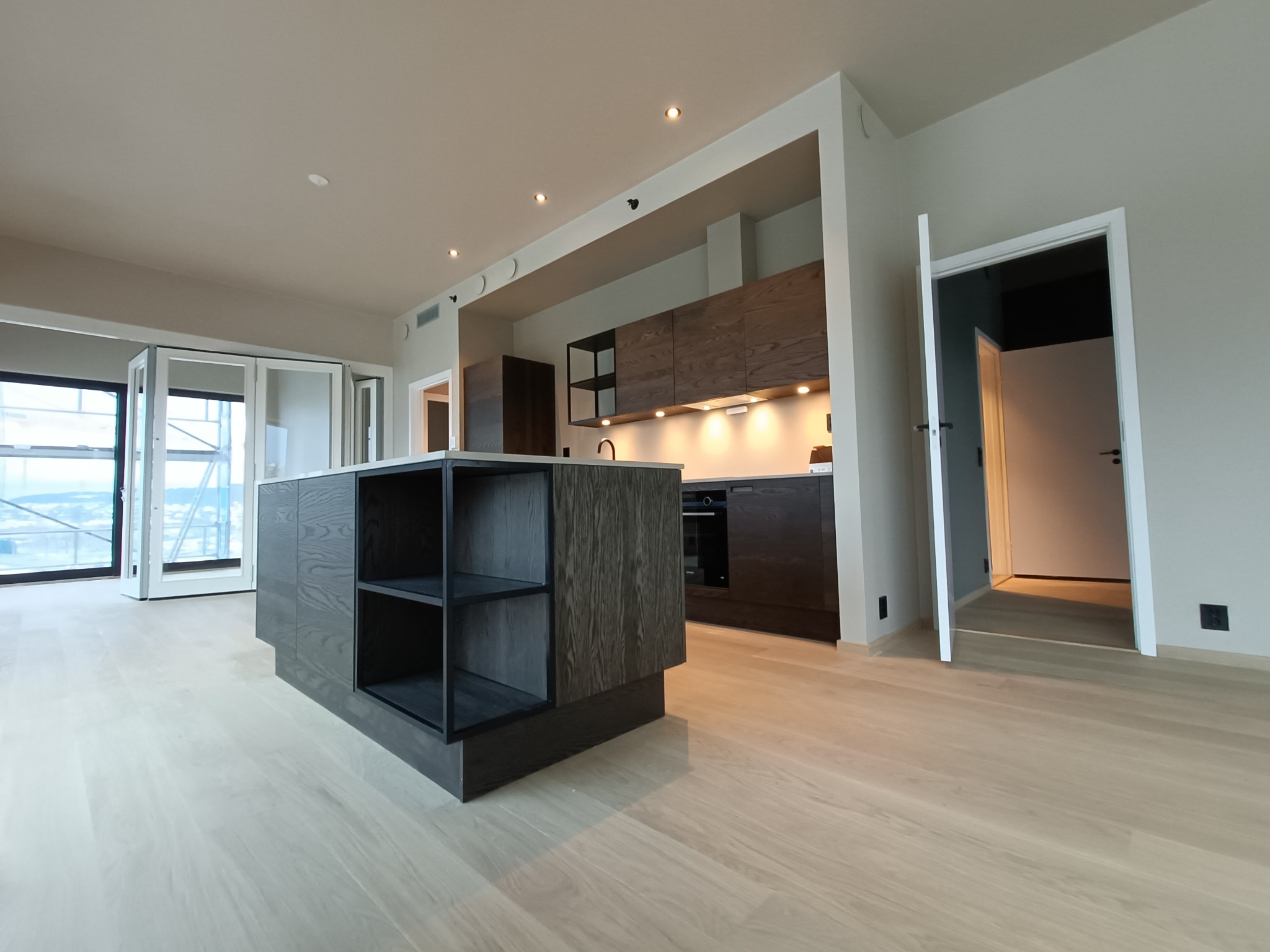 Nowoczesna kuchnia z wyspą i drewnianymi frontami, minimalistyczny design, jasna podłoga, duże okna balkonowe w tle