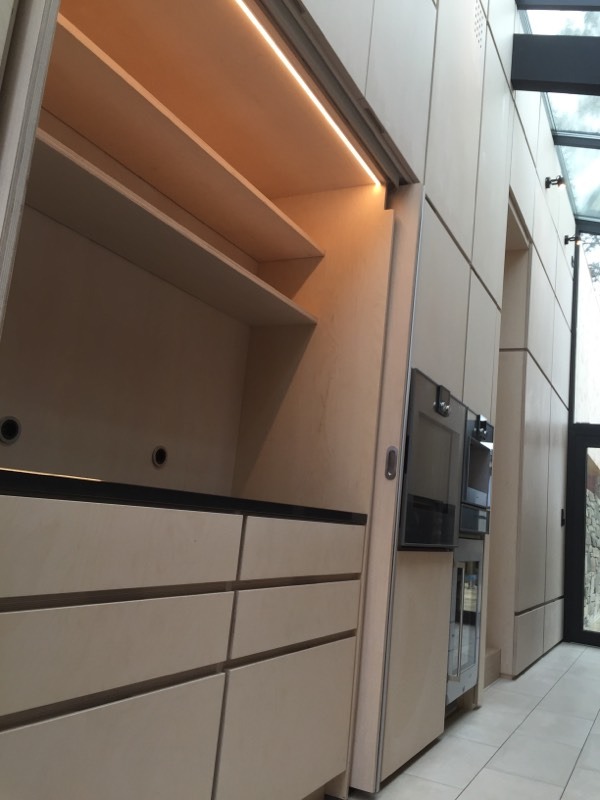 Jasna szafa wnękowa z przesuwnymi drzwiami, oświetleniem LED i szufladami w nowoczesnym wnętrzu z przeszklonym dachem.