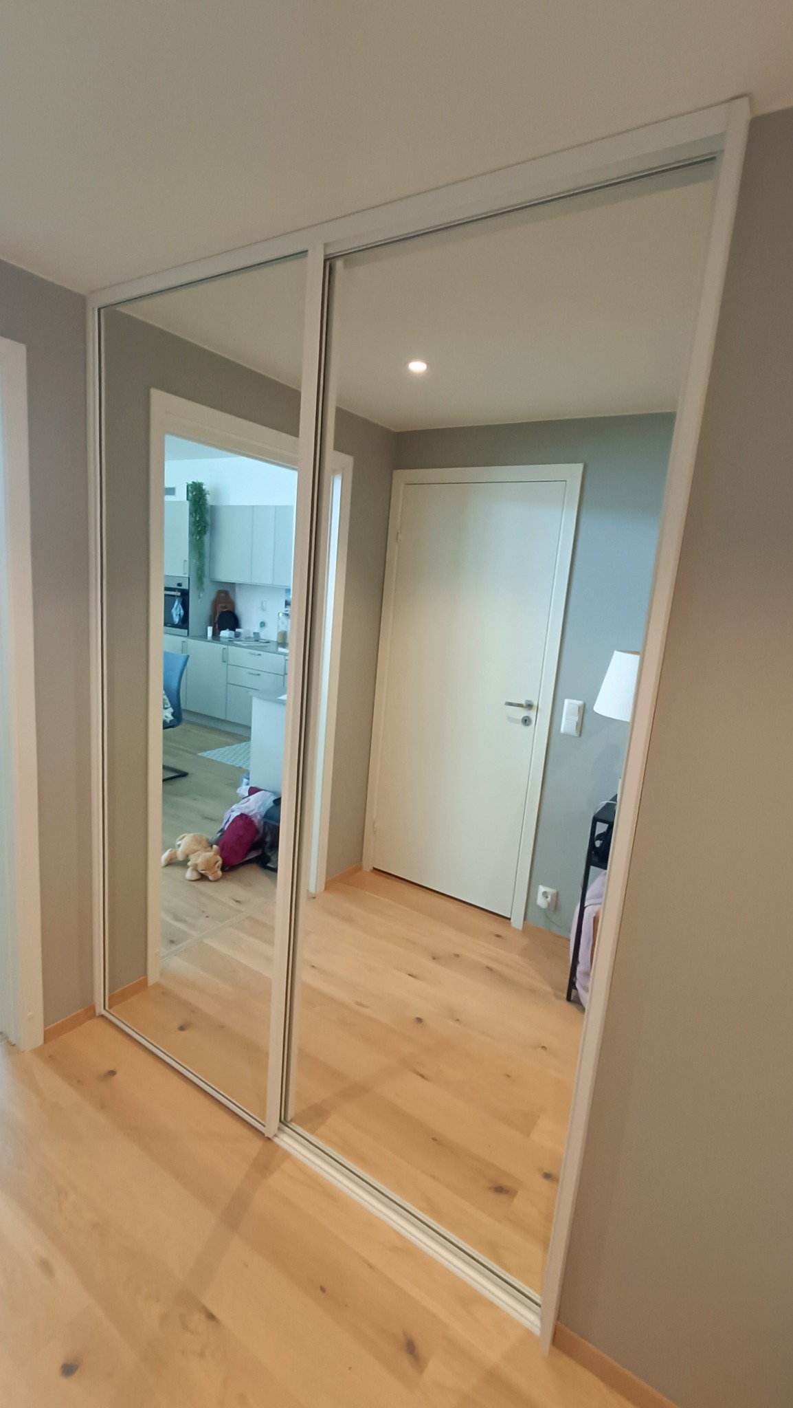 Wbudowana szafa z przesuwnymi drzwiami lustrzanymi, odbijająca wnętrze mieszkania z widoczną kuchnią i częścią pokoju z drewnianą podłogą.