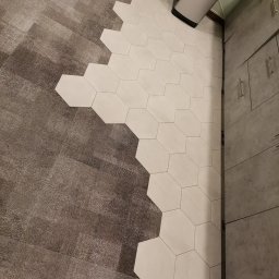 Garant-BUD - Połączenie wykładziny dywanowej i heksagonalnych płytek podłogowych w odcieniach szarości, widok z góry, fragment szafki kuchennej w tle.