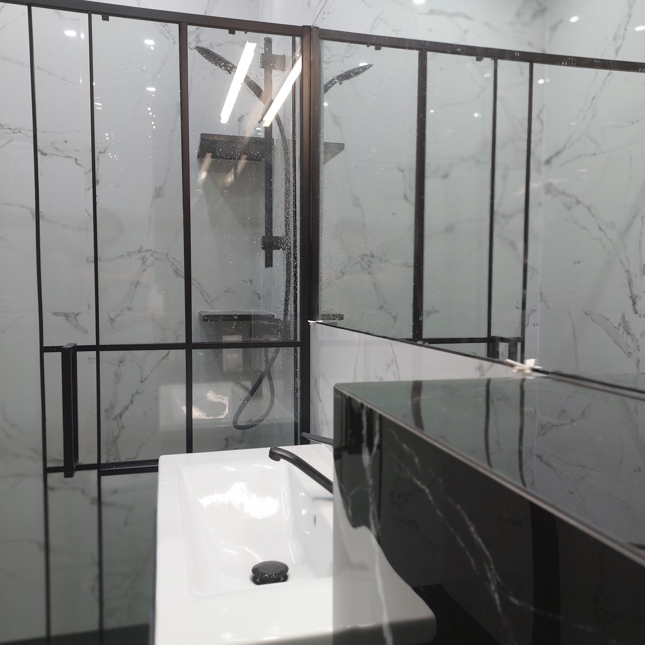 Nowoczesna łazienka z kabiną prysznicową typu walk-in, czarną armaturą i umywalką nablatową, wykończona marmurowymi płytkami.