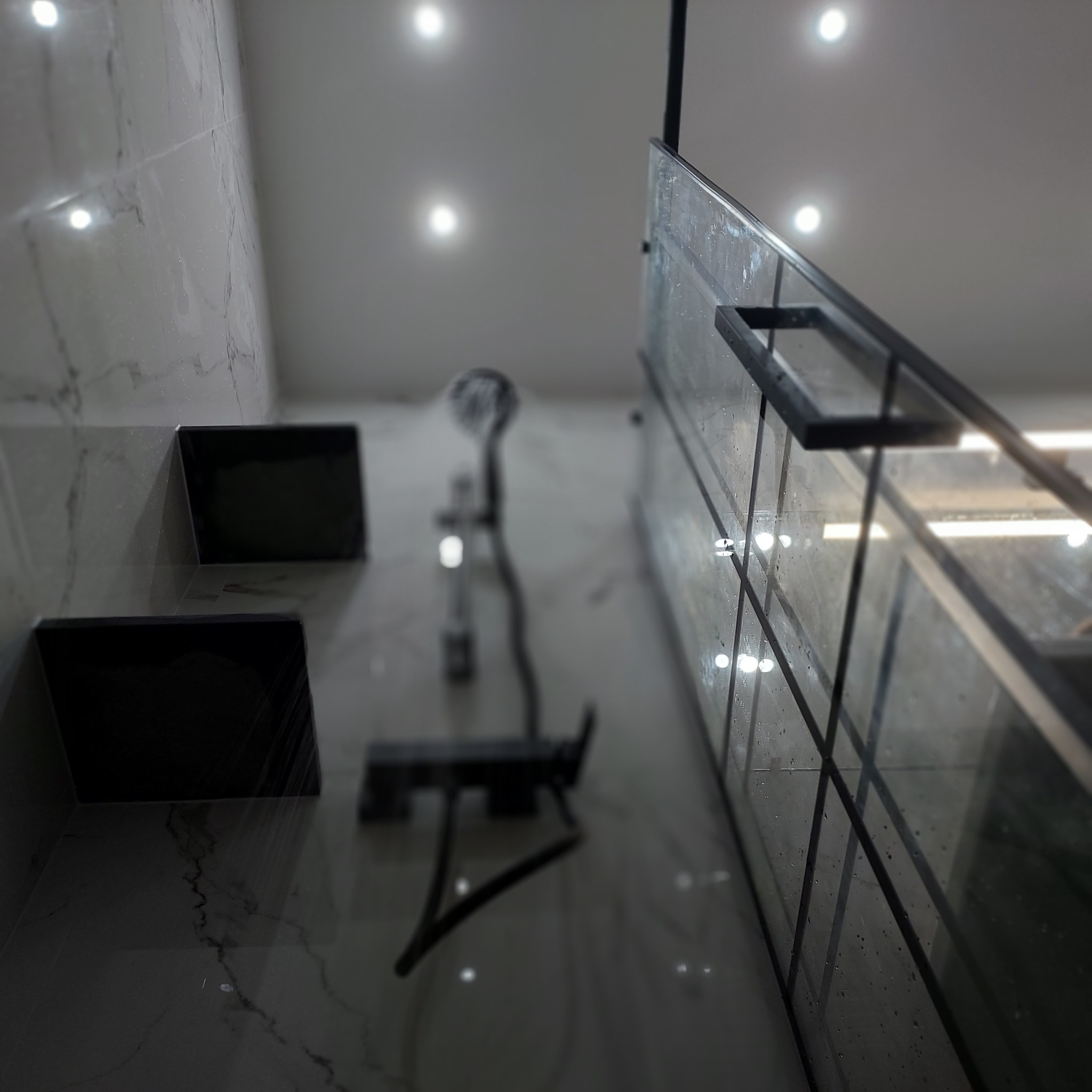 Nowoczesna kabina prysznicowa z czarnymi profilami i armaturą, widok z dołu, marmurowe płytki na ścianach i podłodze, minimalistyczne półki wbudowane w ścianę.