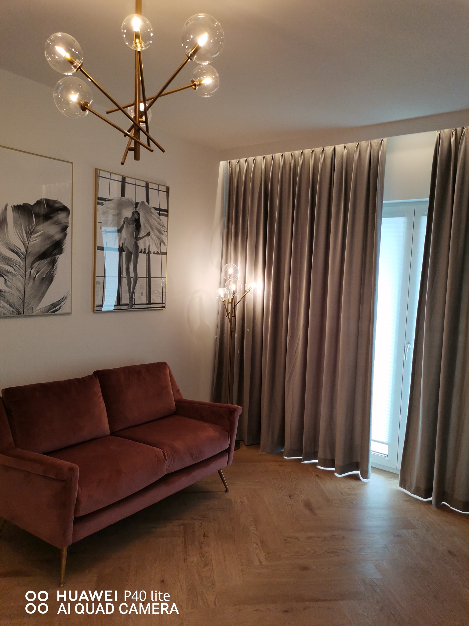 Nowoczesny salon z parkietem w jodełkę, bordową sofą, szarymi zasłonami i designerską lampą sufitową.